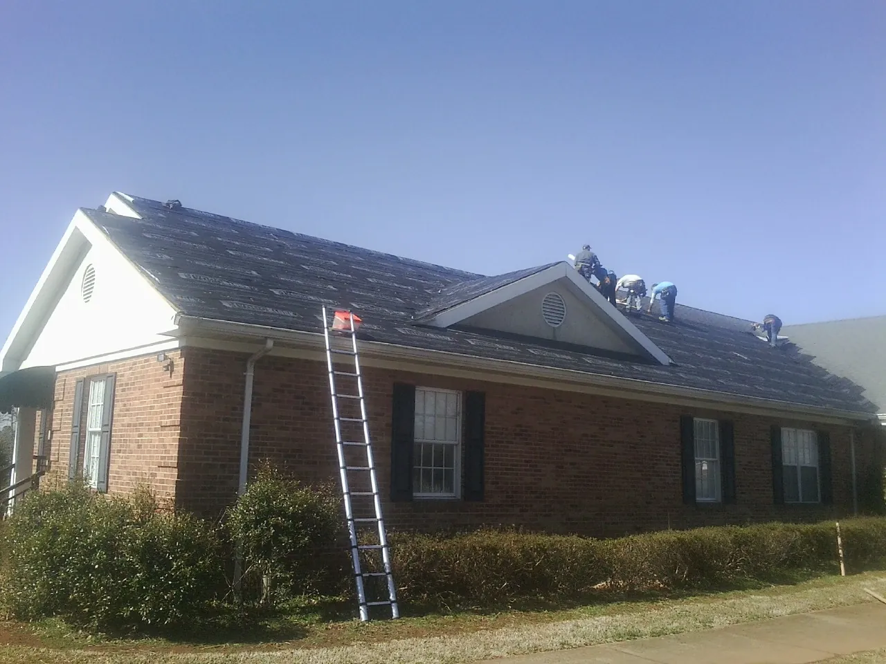 Crew tearing shingles off a brick ranch roof with a ladder set — Emergency Roof Repair work by our crew in Rehoboth