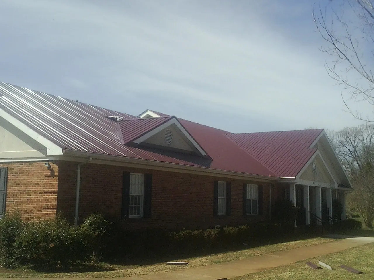 Red metal roof with gabled entries on a long brick building, from a Hail Damage Roof Repair job in Rehoboth