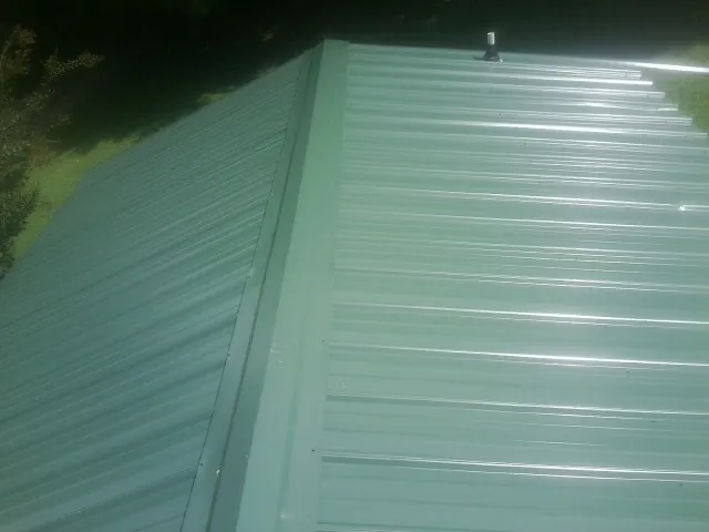 New green metal panels meeting at the ridge of a roof — Flat Roof Repair work by our crew in Rehoboth