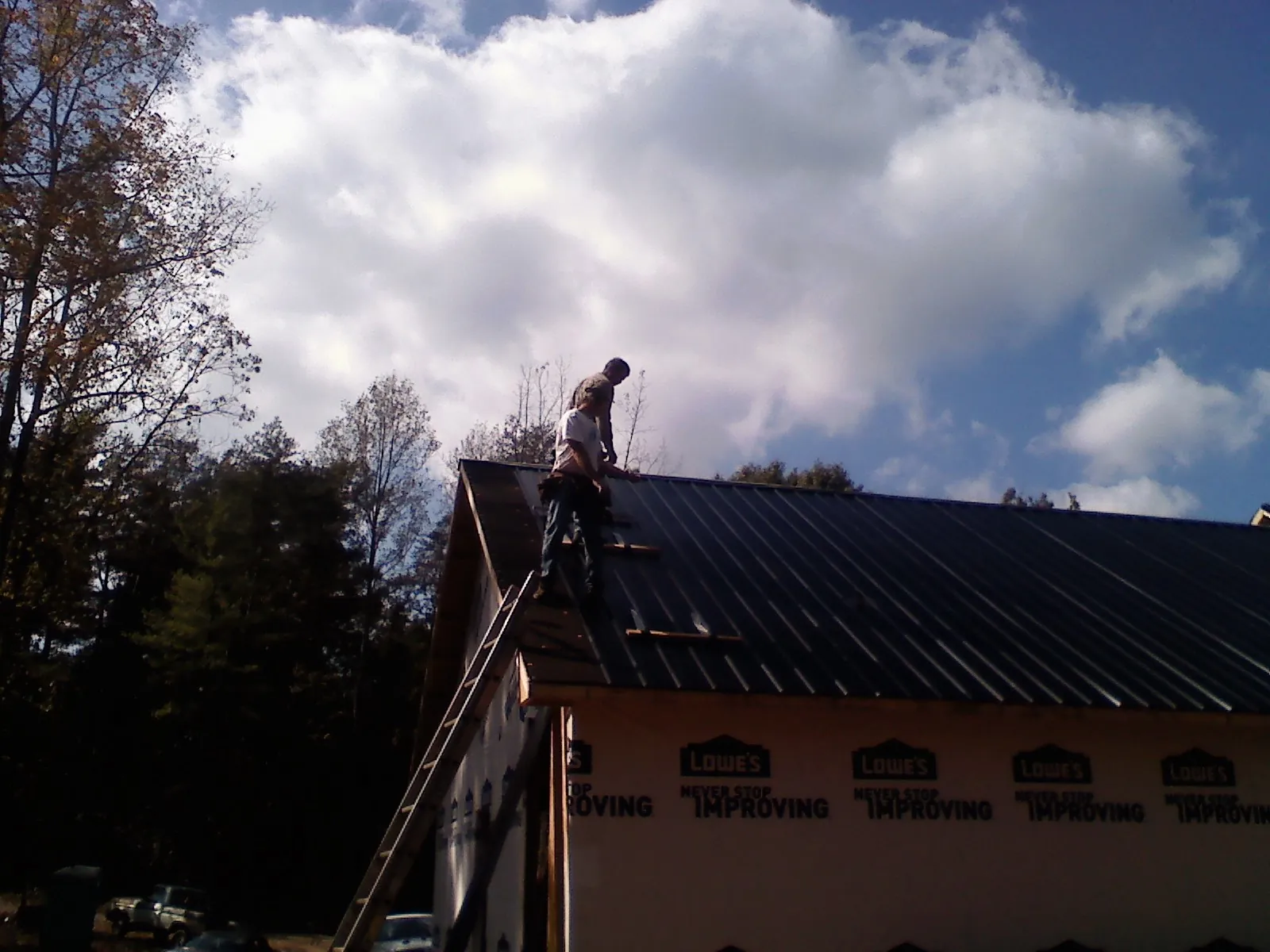 Roofer fastening dark metal panels high against a cloudy sky, from a Roof Inspection job in Rehoboth