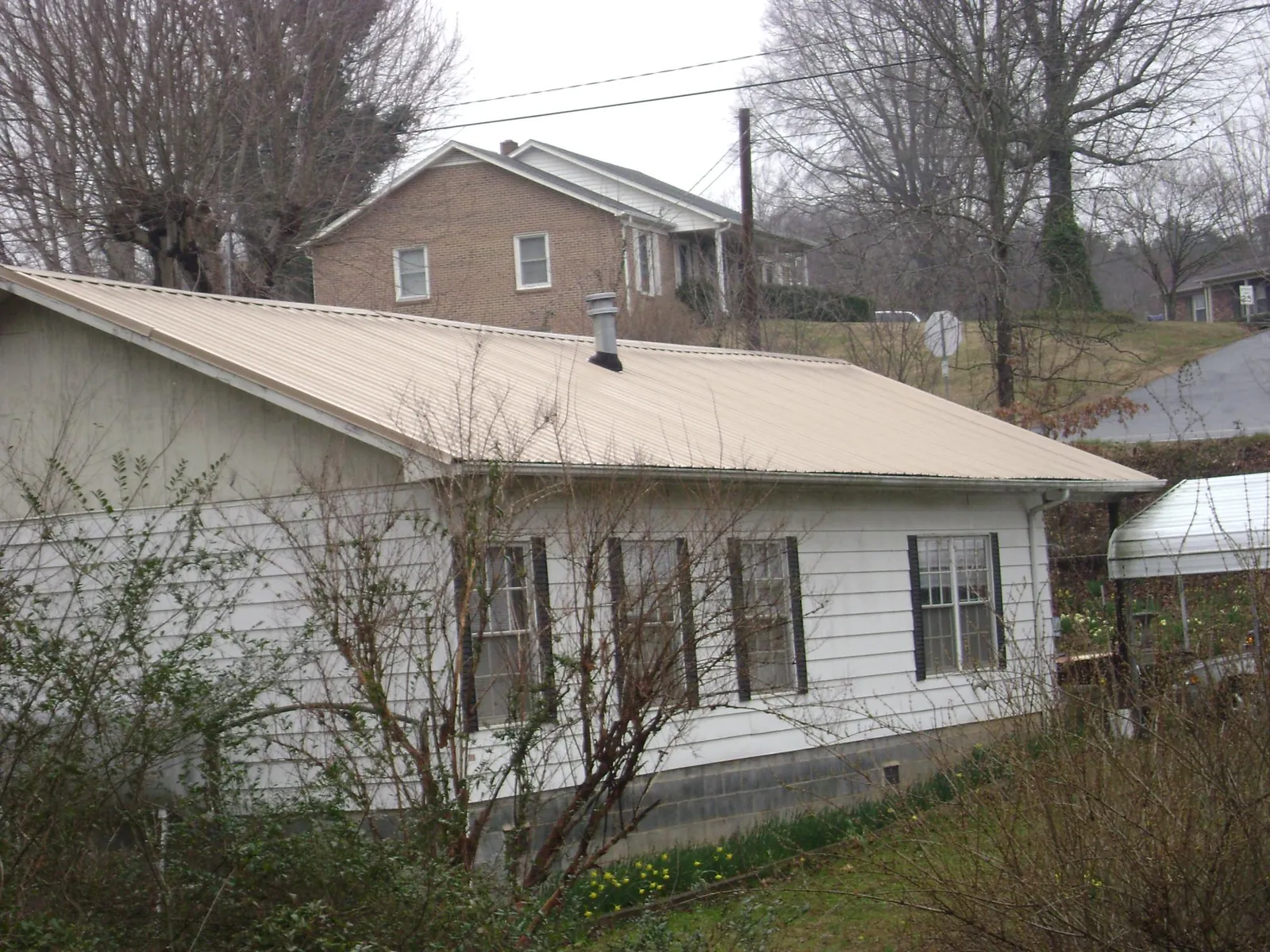 Tan metal roof on a white sided house set into a hillside — Commercial Roofing by Roofing Brothers in Rehoboth