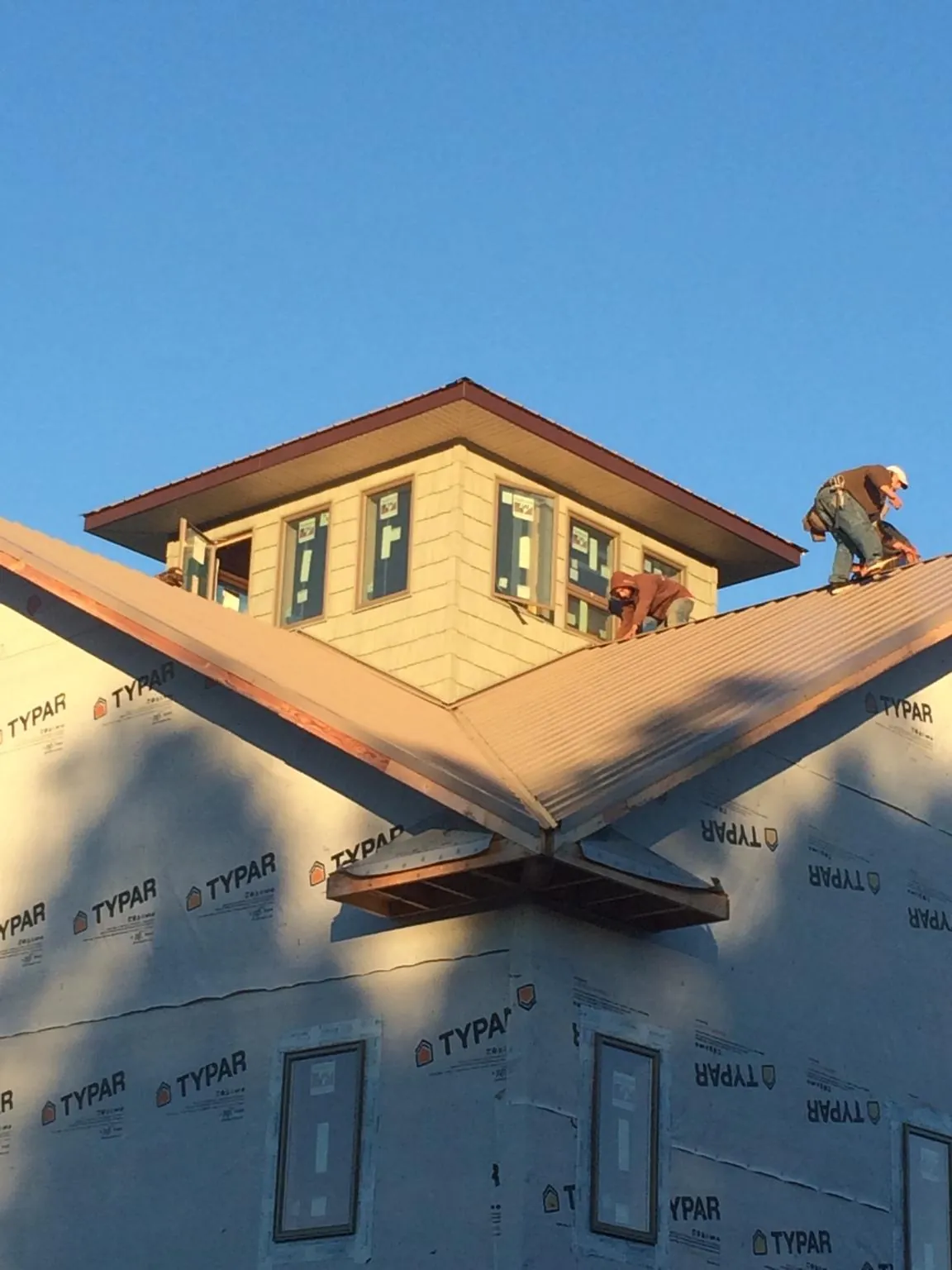 Roofers working around a rooftop cupola on a new metal roof at sunset — Roof Waterproofing in Rehoboth by Roofing Brothers